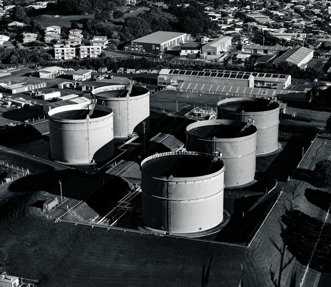 Black and white aerial view of industrial storage tanks surrounded by urban landscape, showcasing industrial infrastructure.